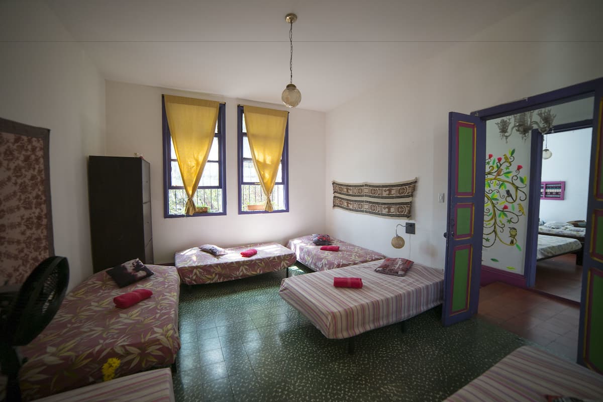 A room with three beds, a fan, and a window with yellow curtains.