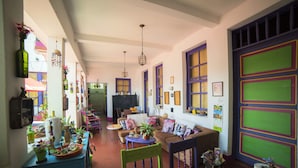 Una sala de estar acogedora con un sofá, sillas y una mesa de centro. Hay plantas, un televisor y una estantería.