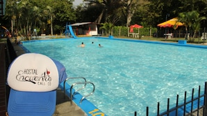 Una piscina con gente nadando, un puesto de socorrista y una valla azul.