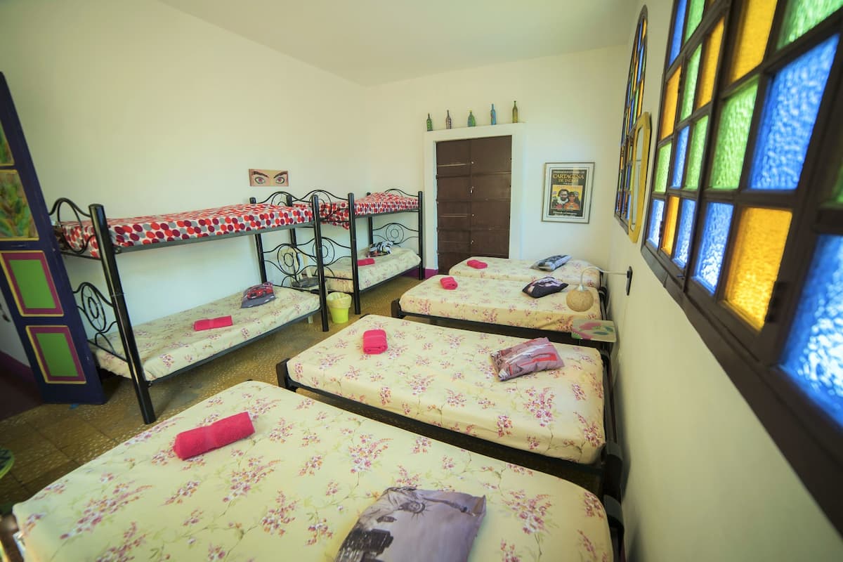 A dormitory room with four bunk beds, a door, and a window with stained glass.