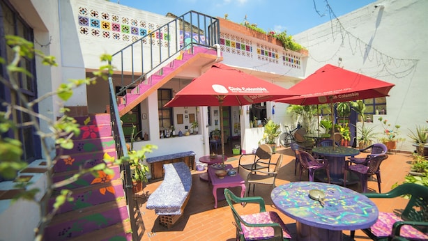 Un patio con mobiliario de colores, una escalera y asientos al aire libre bajo sombrillas rojas.