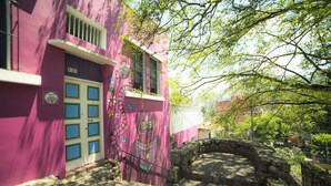 Un edificio rosa con un mural de un búho, un muro de piedra y un pequeño puente.