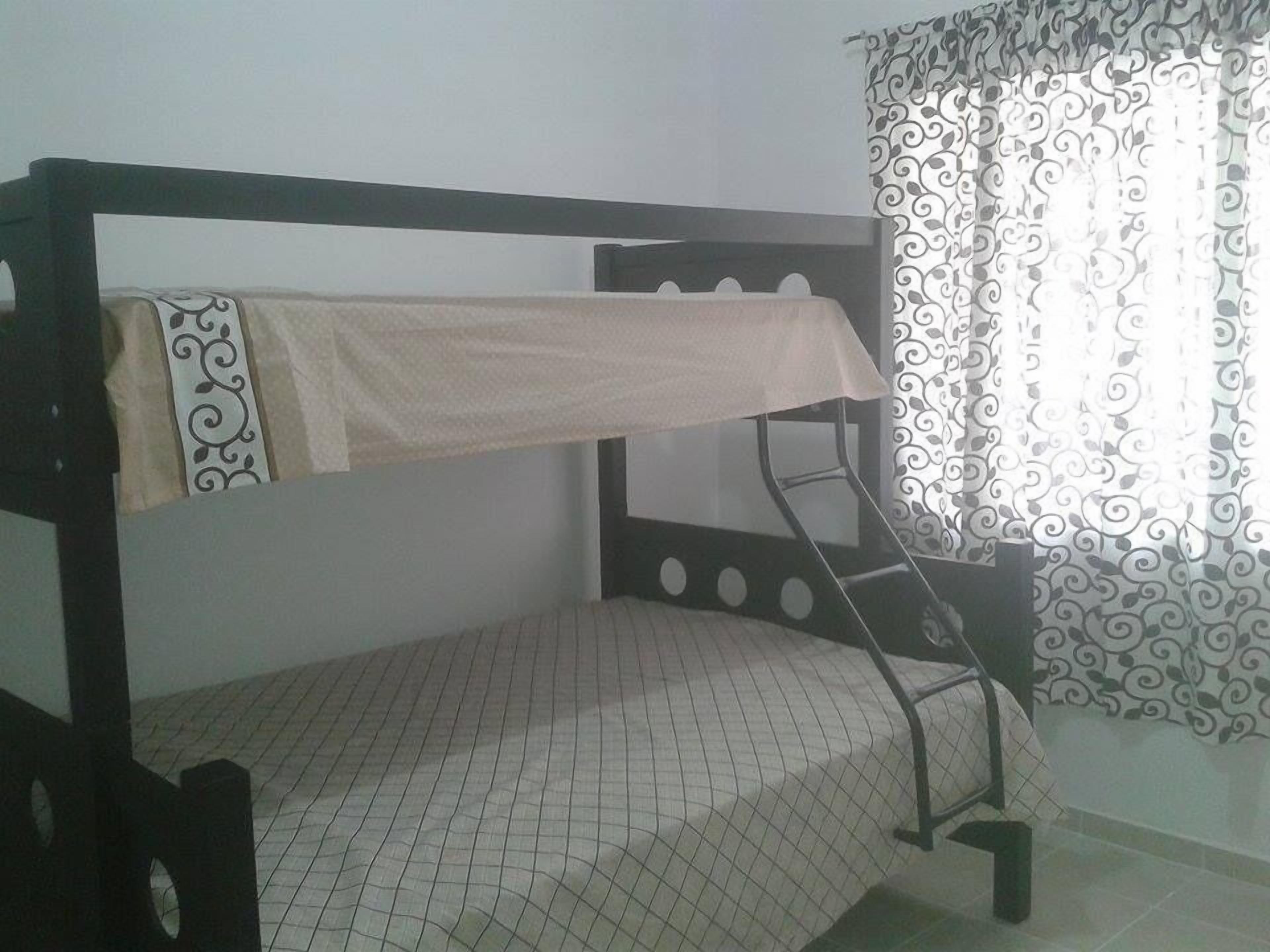 A bunk bed with a patterned mattress, a small stool, and a window with decorative curtains.