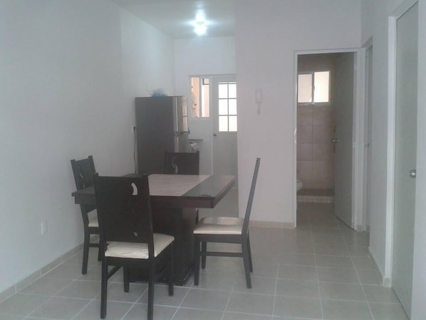 A dining area with a rectangular table and four chairs, a cabinet, and a door leading to a bathroom.