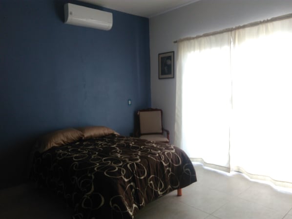 A bedroom with a bed, a chair, a picture on the wall, and a window with curtains.