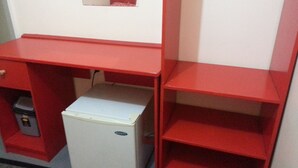 Een compacte kamer met een rode bureau, een witte minibar en een kleine prullenbak.