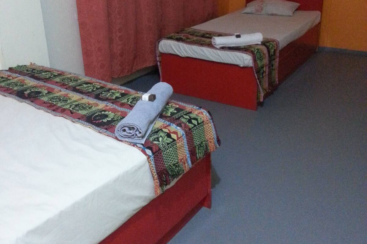 A room with two single beds, each with a patterned bedspread and a rolled towel.