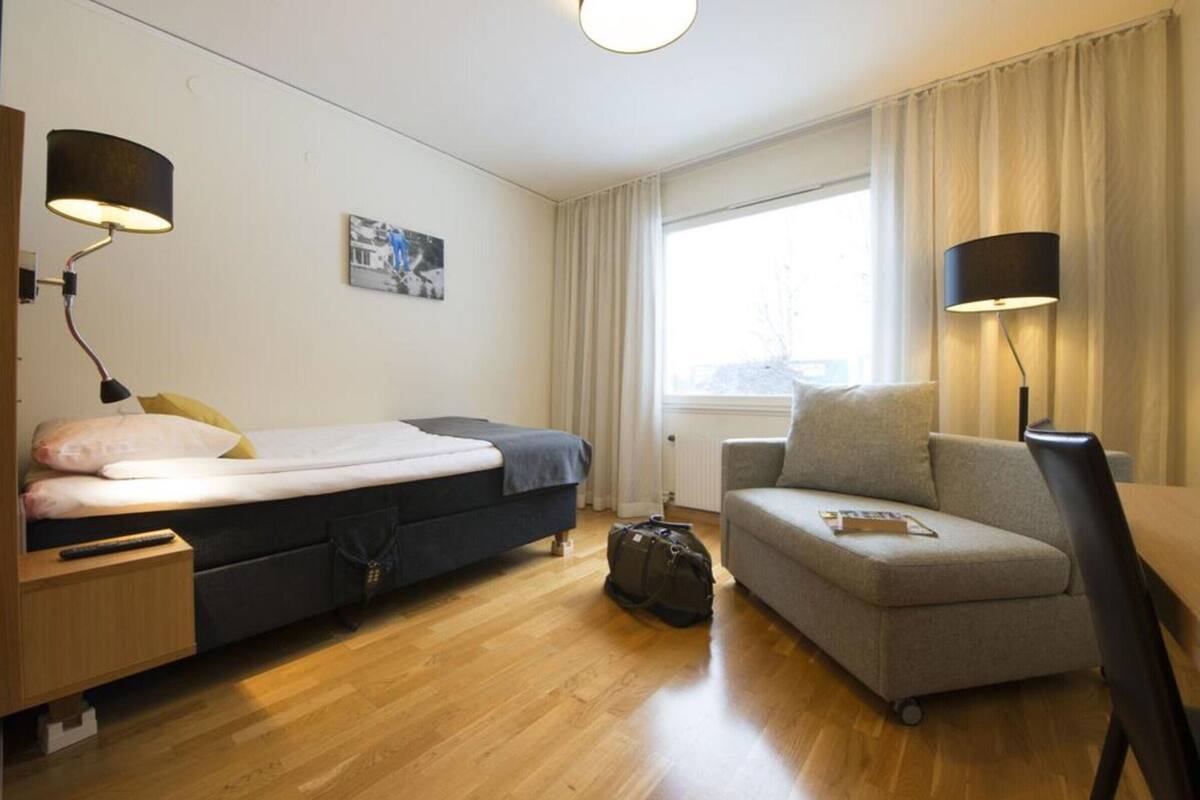 A compact hotel room with a bed, a sofa, a desk, and a lamp.