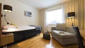 Ett kompakt hotellrum med en säng, en soffa, ett skrivbord och en lampa.