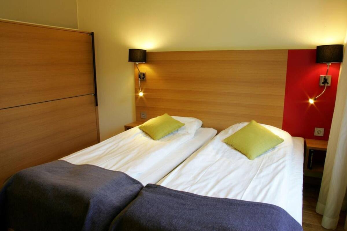 A hotel room with two single beds, each with a pillow and a bedside table.