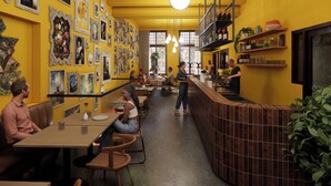Een restaurant met gele wanden, houten tafels en een bar met flessen op planken.