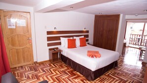 A hotel room with a wooden headboard, a bed with white and orange bedding, a wooden floor, a nightstand, and a red curtain. - Hotel Arcangel (Cusco)