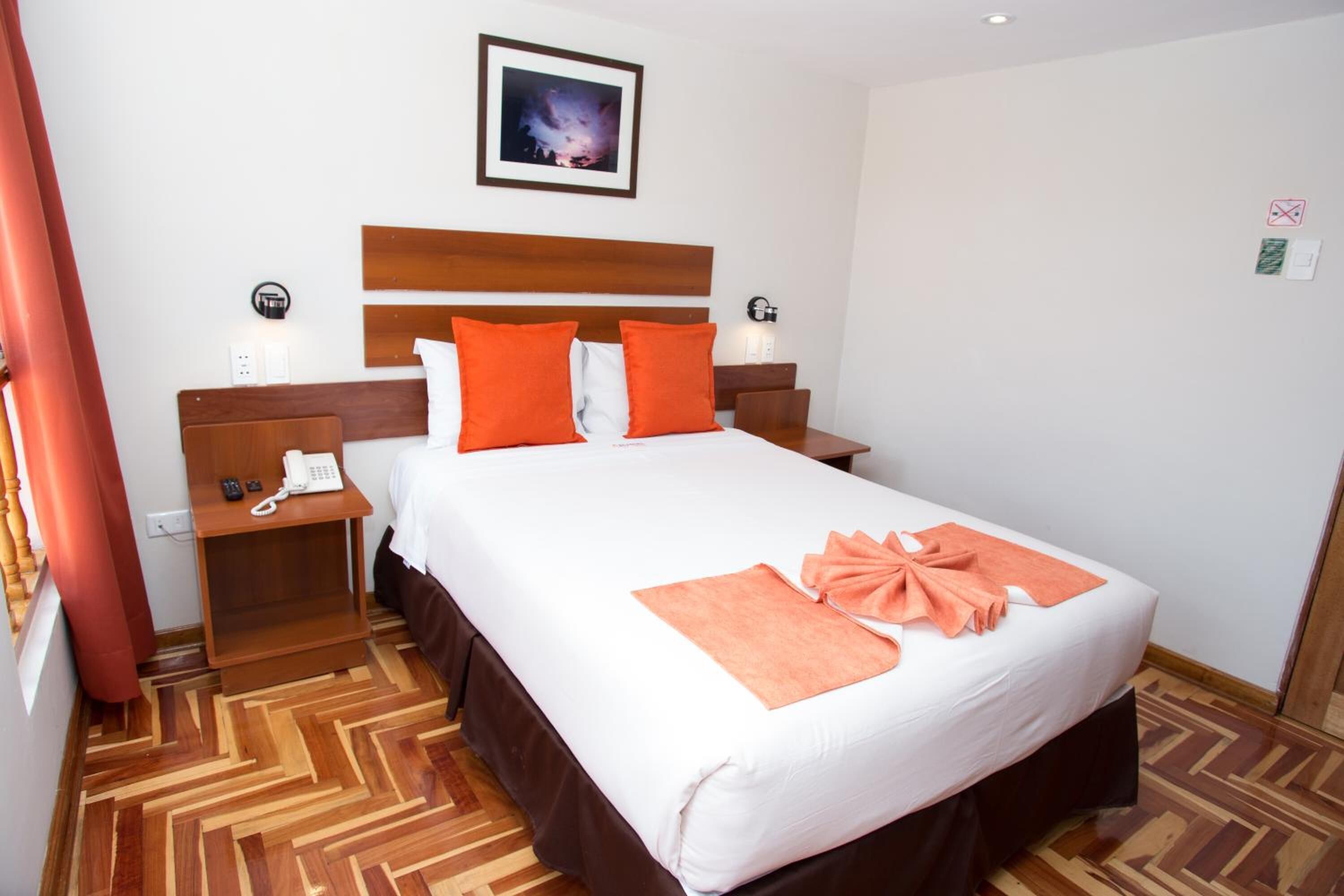 Habitación de hotel con una cama grande, cabecero de madera, dos mesitas de noche, un teléfono y un cuadro en la pared.