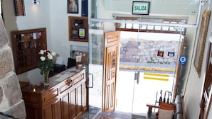 A lobby with a reception desk, a staircase, a bench, and a glass door leading outside. - Hotel Arcangel (Cusco)