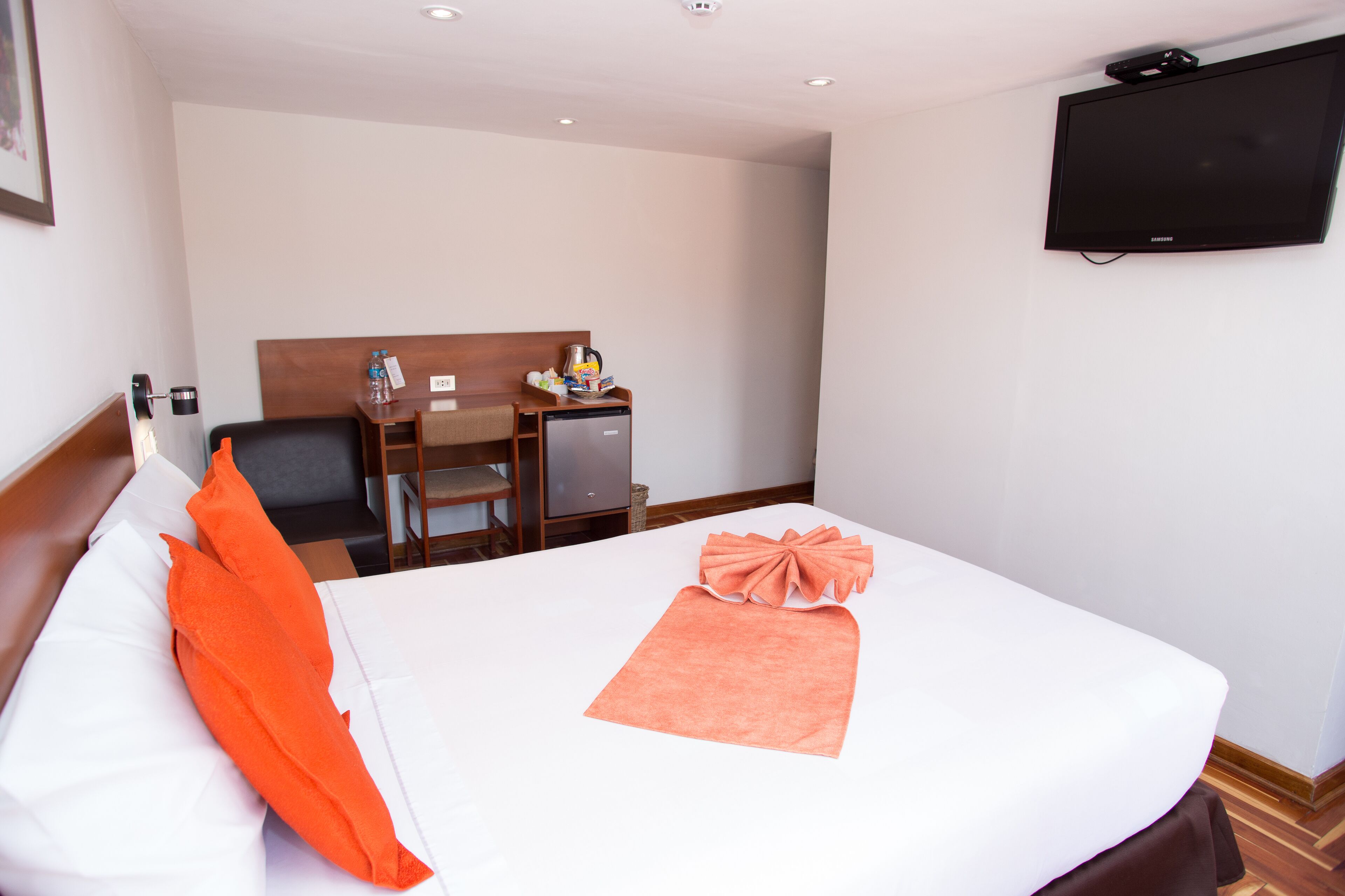 Una habitación de hotel con cama, escritorio, silla, televisor y un pequeño refrigerador.