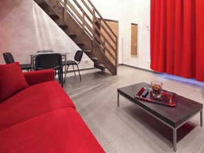 A modern living room with a red sofa, a glass coffee table with a tray, a staircase, and a red curtain. - Residence Maximus (Rome)