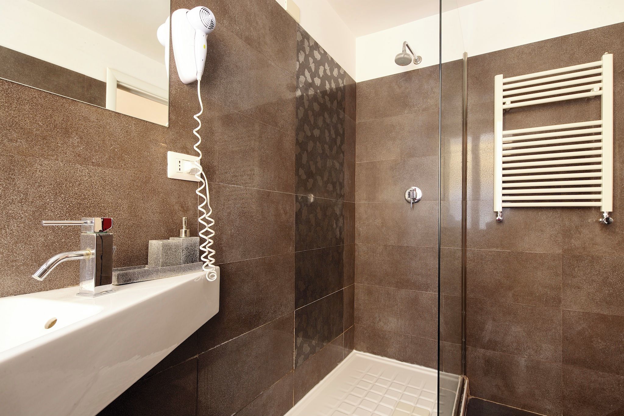 Un bagno moderno con box doccia in vetro, un lavandino bianco con rubinetto cromato e un porta asciugamani.