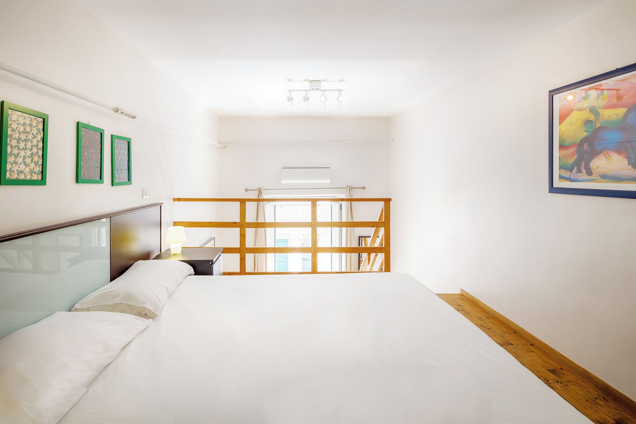 Habitación de hotel con cama, escritorio, silla, ventana y obras de arte en las paredes.