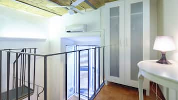 Eine Treppe führt zu einem Balkon mit Blick auf ein Gebäude. Auf dem Balkon steht ein Tisch mit einer Lampe.