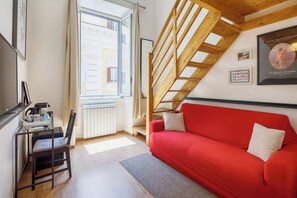 A cozy room with a red sofa, a wooden staircase, and a window with curtains. - Residence Maximus (Rome)