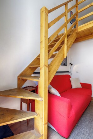 A wooden staircase leading to a red sofa in a room with white walls.