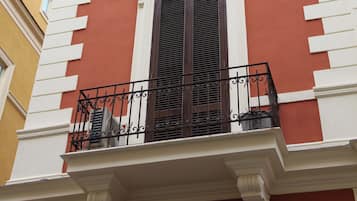 Un edificio con balcón, una ventana con contraventanas y una cornisa decorativa.