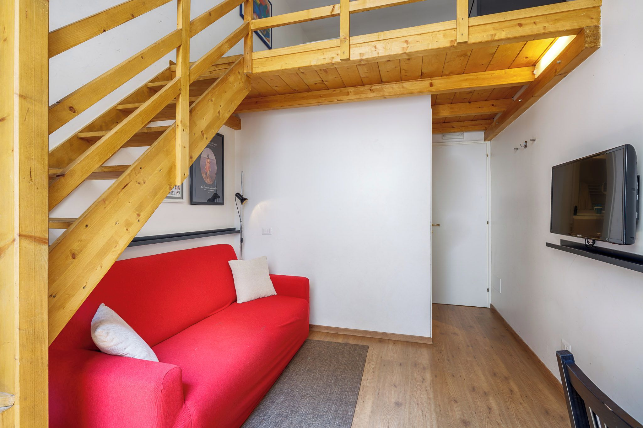 A room with a red sofa, wooden staircase, and a mounted TV.