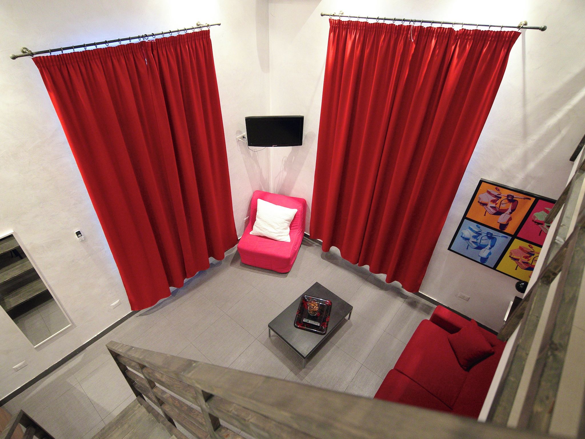 A room with red curtains, a pink chair, a small table, and a colorful artwork on the wall.