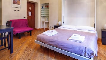 Une chambre à coucher avec un lit, un bureau, une chaise et une petite table sur laquelle se trouve un vase.