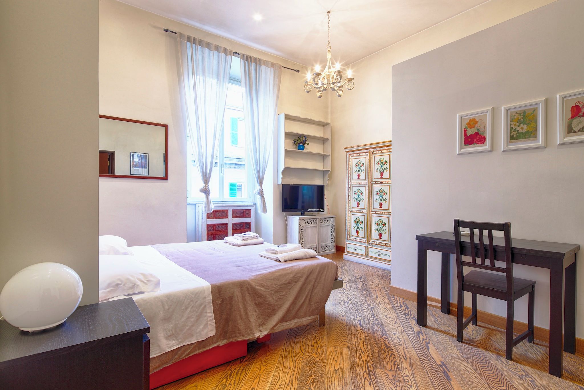 Una camera d'albergo con un letto, una scrivania, una sedia, una televisione e un lampadario.