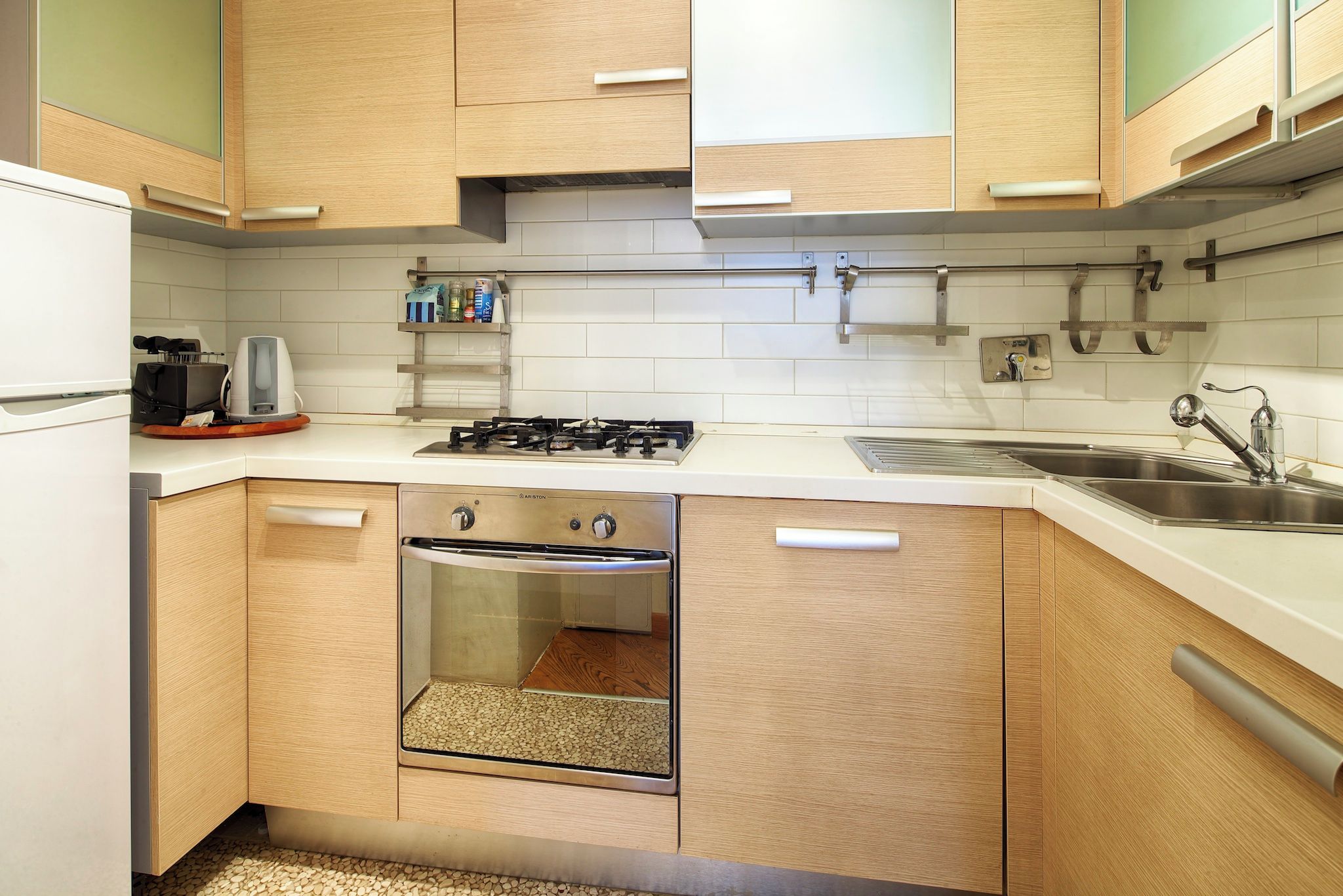 Una cucina compatta con mobili in legno, forno integrato, piano cottura a gas e lavello in acciaio inossidabile.