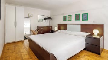 Ein Schlafzimmer mit großem Bett, Holzboden, Kleiderschrank, Nachttisch mit Lampe und Wandbildern.