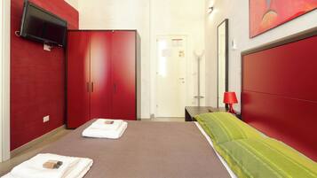 Habitación de hotel con cama, armario rojo y televisor montado en la pared.