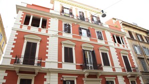 Un edificio de varios pisos con fachada roja y blanca, múltiples balcones y un estilo arquitectónico tradicional.