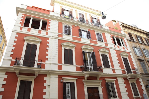 Un immeuble à plusieurs étages, doté d’une façade rouge et blanche, de nombreux balcons et d’un style architectural traditionnel.