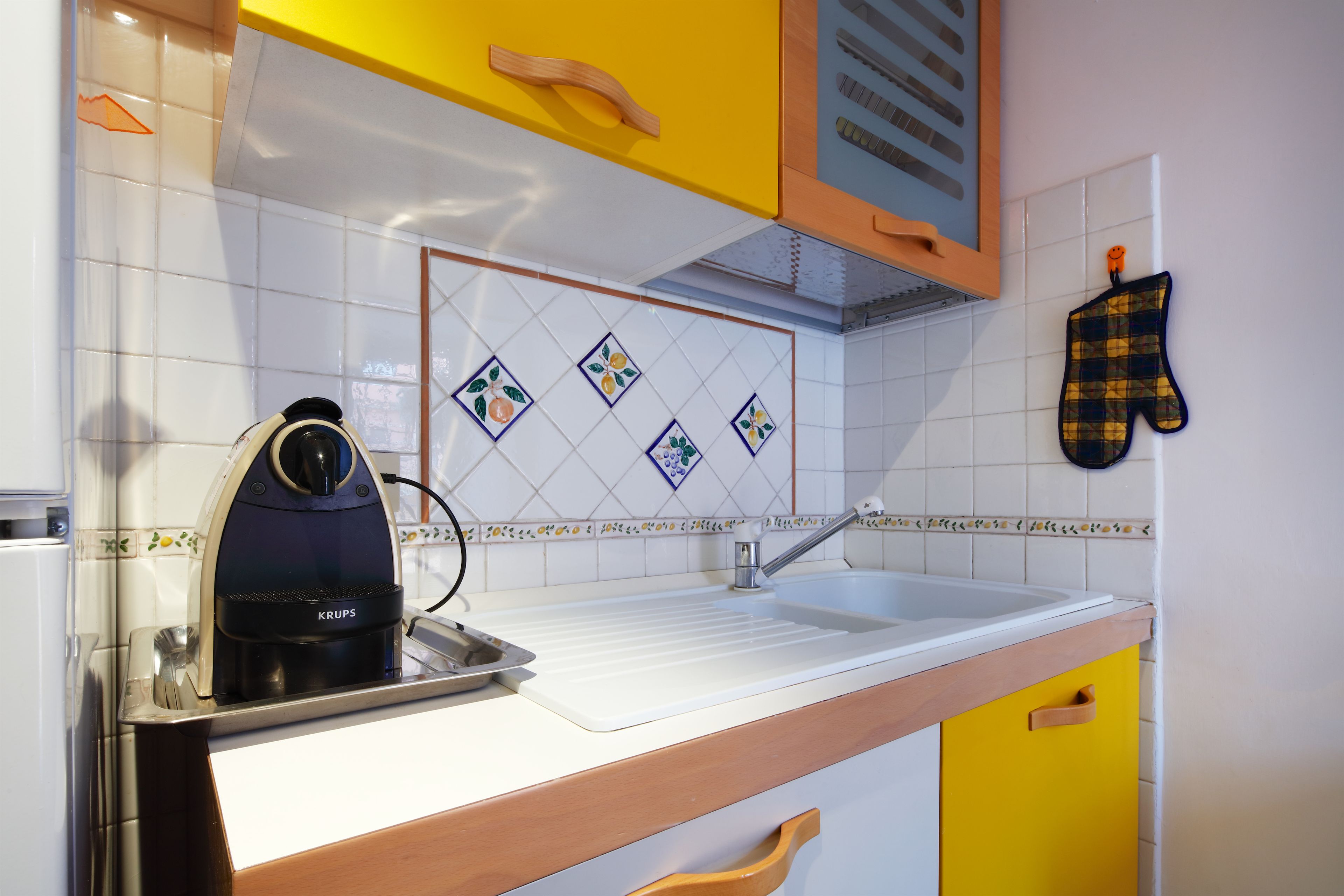 Una cocina con hervidor, pileta y salpicadero con diseños de frutas.