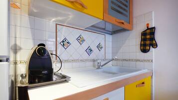 Una cocina con hervidor, pileta y salpicadero con diseños de frutas.