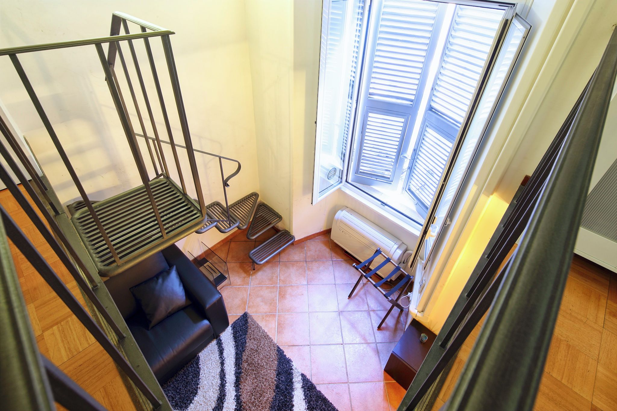 Une pièce avec un escalier, un canapé, un radiateur et une fenêtre avec des stores.