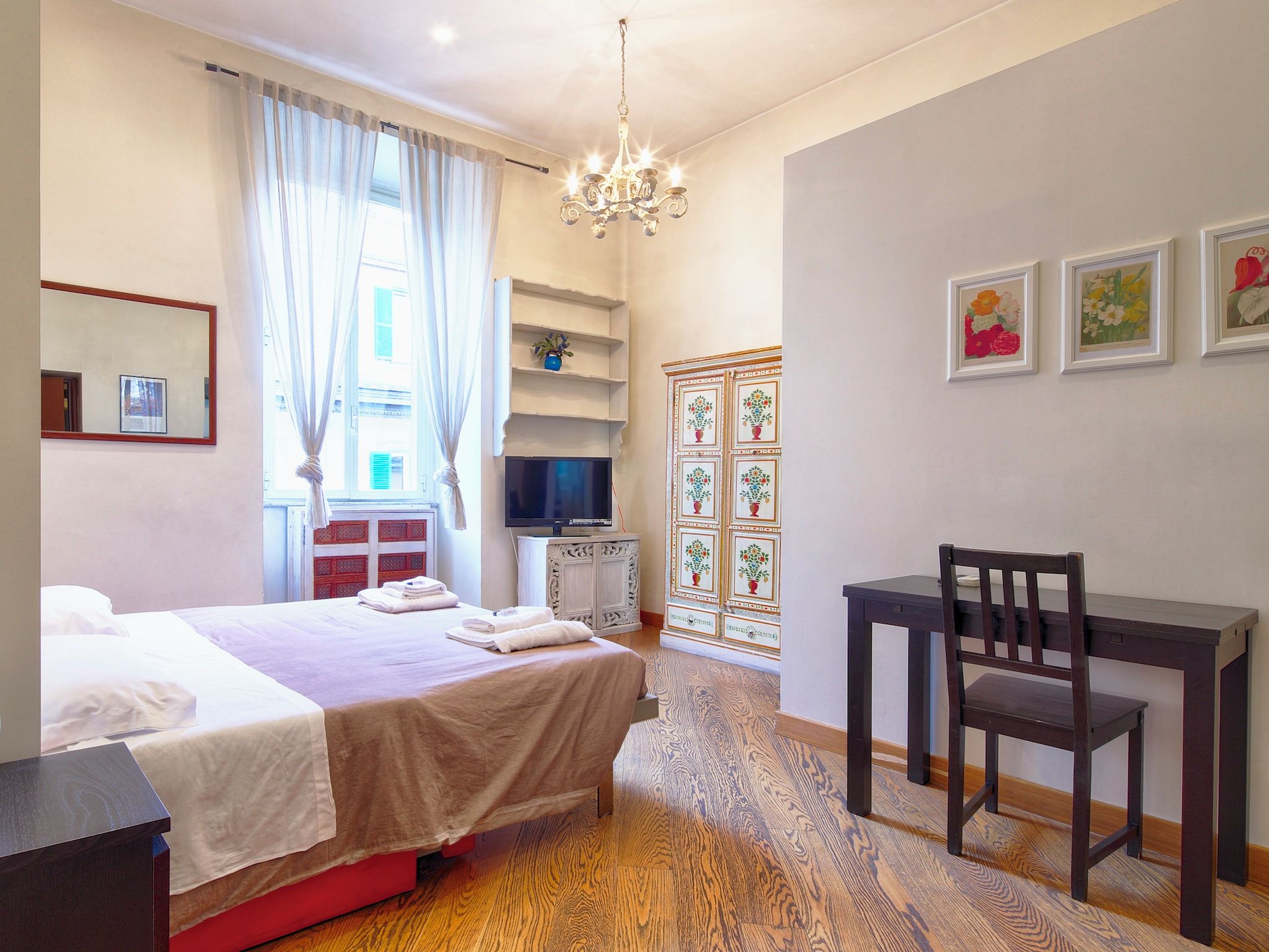Une chambre d’hôtel équipée d’un lit, d’un bureau, d’une chaise, d’une télévision et d’un lustre.