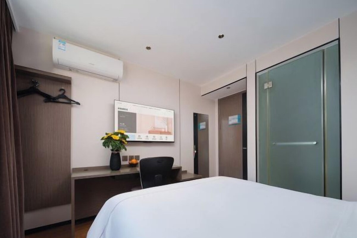 A hotel room with a bed, a desk with a computer, a wardrobe, and a mirror.