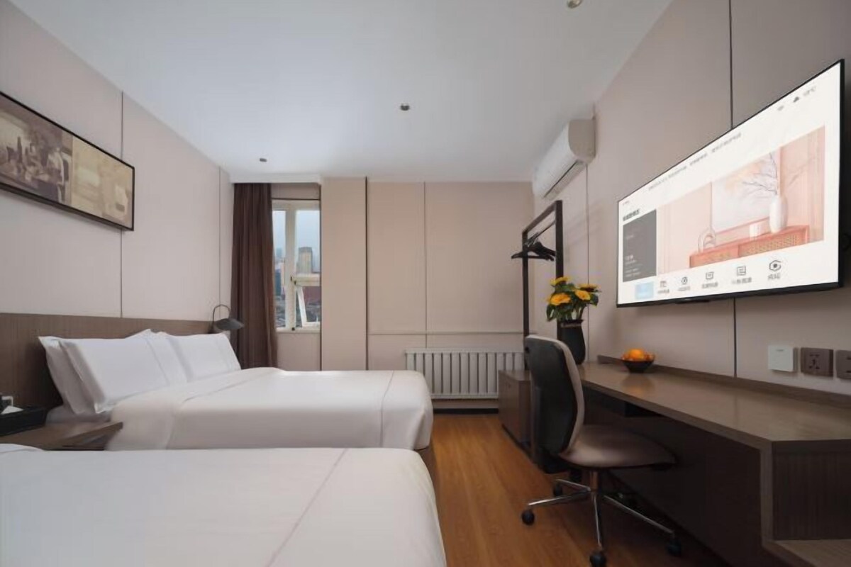 A hotel room with two beds, a desk, a chair, a TV, and a window.