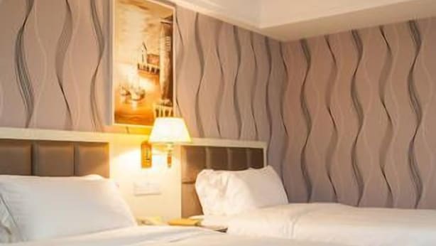 A hotel room with two beds, a headboard, a wall-mounted lamp, and a framed picture. - Hanmu Lanting Holiday Hotel (Nantong)
