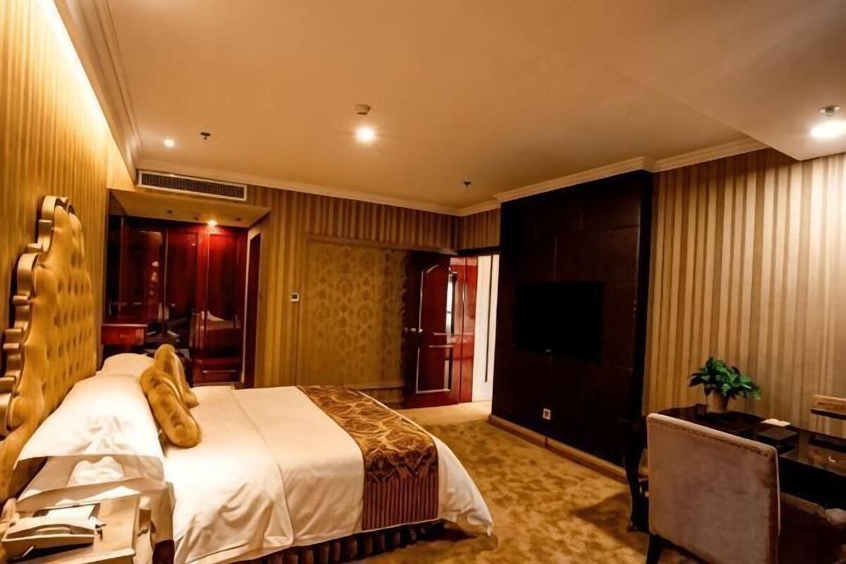 Una habitación de hotel con cama, escritorio, silla, televisor y armario.