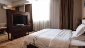 Et hotelværelse med en stor seng, et fladskærms-TV og et vindue med gardiner.