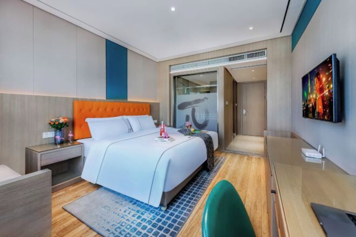A modern hotel room with a large bed, a desk, and a TV on the wall.