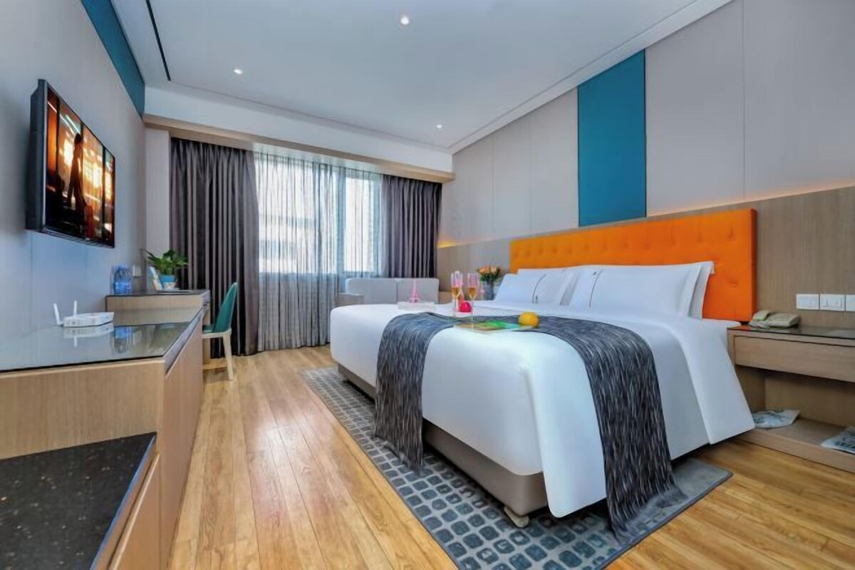 A modern hotel room with a large bed, a desk, a TV, and a view of the city.