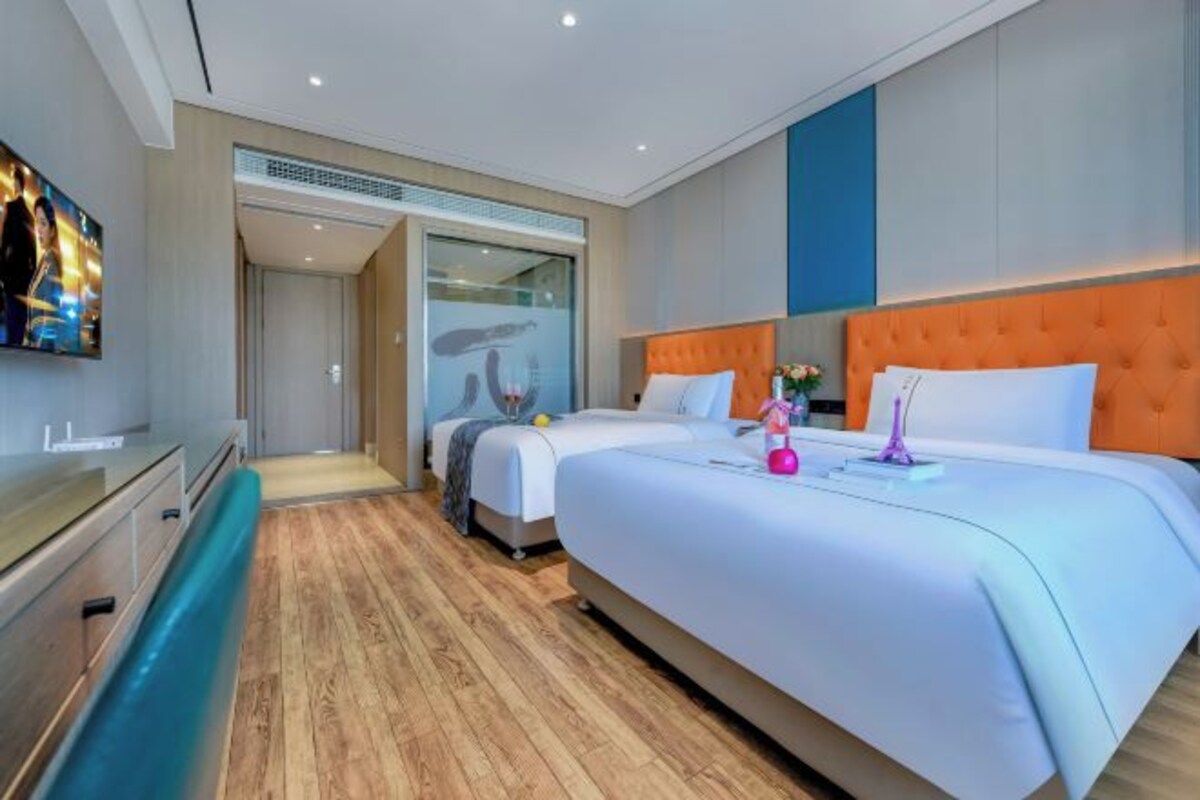 A hotel room with two beds, a TV, a bathroom, and a wooden floor.