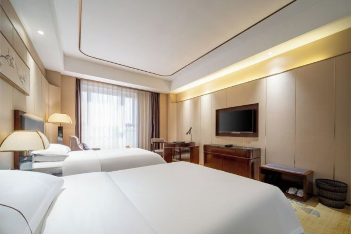 Une chambre d’hôtel avec deux lits, un bureau, une chaise, une télévision et une fenêtre avec des rideaux.