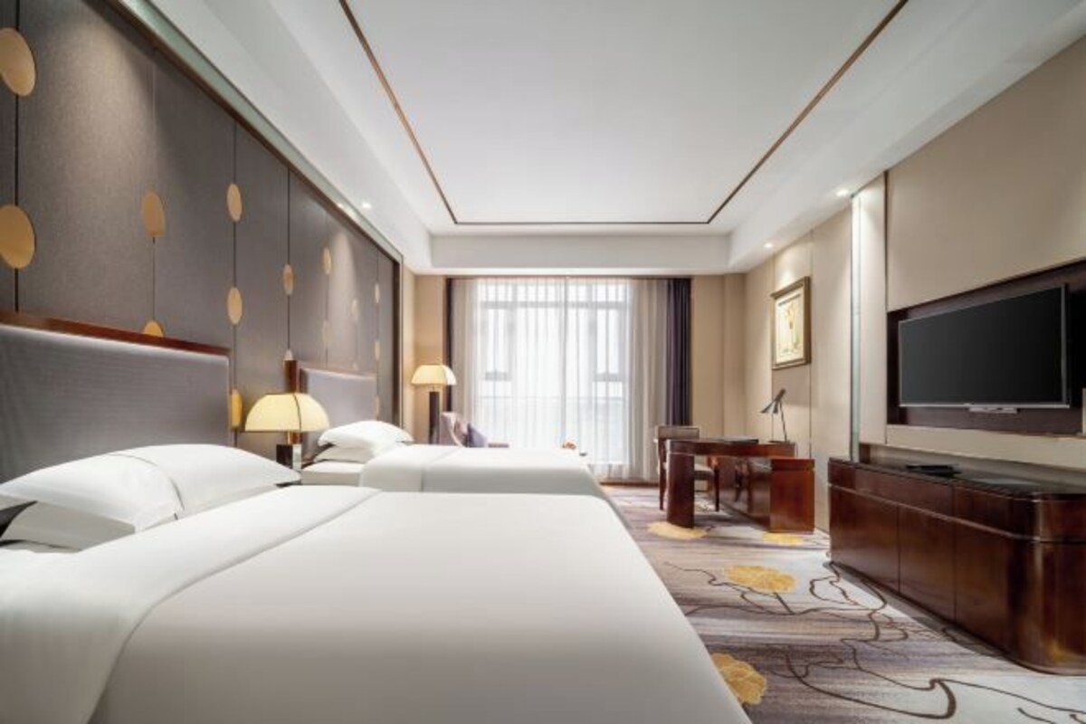 Une chambre d’hôtel avec deux lits, un bureau, une télévision et une grande fenêtre avec des rideaux.