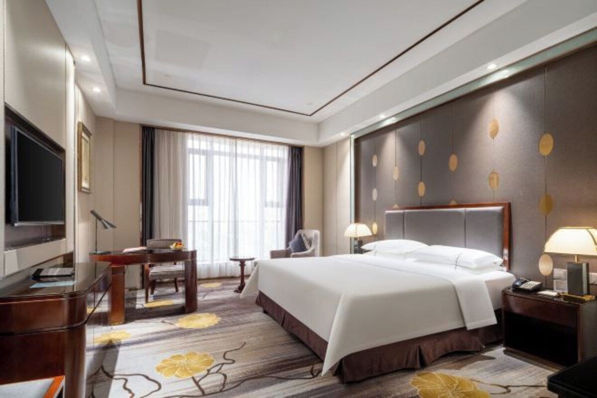 Une chambre d’hôtel avec un grand lit, un bureau, une chaise, une télévision et une fenêtre avec des rideaux.